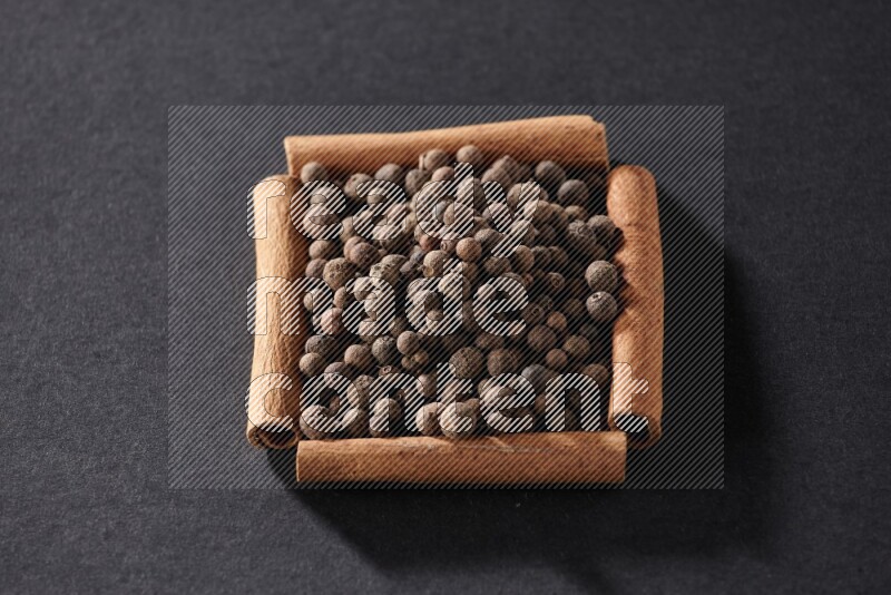 A single square of cinnamon sticks full of allspice on black flooring