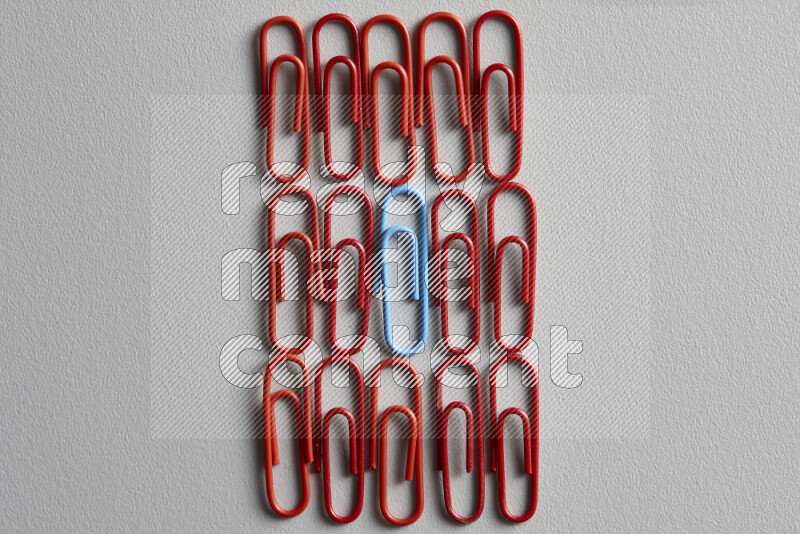 A blue paperclip surrounded by bunch of red paperclips on grey background