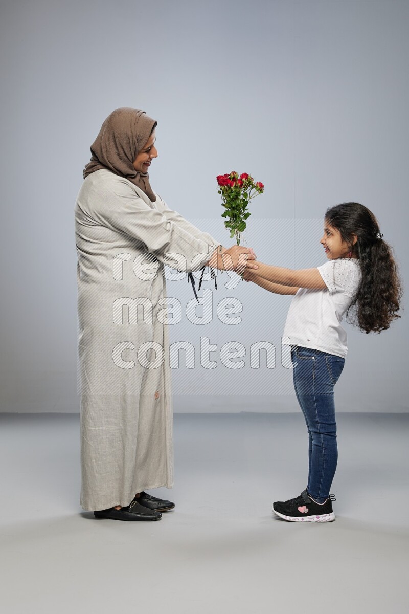 A girl standing giving flowers to her mother on gray background