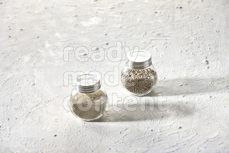 وعاءين زجاجيين عشبيين ممتلئين بحبوب وبودرة الفلفل الأبيض على أرضية بيضاء