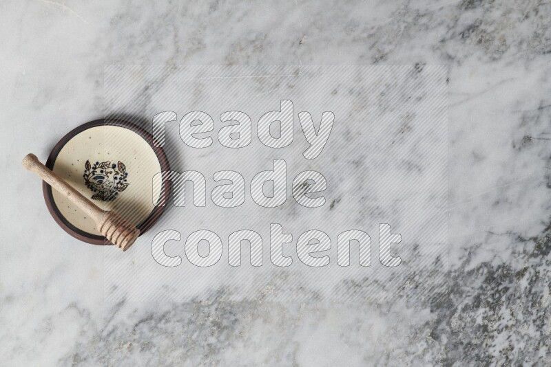 Decorative pottery plate with wooden honey dipper in it on grey marble background