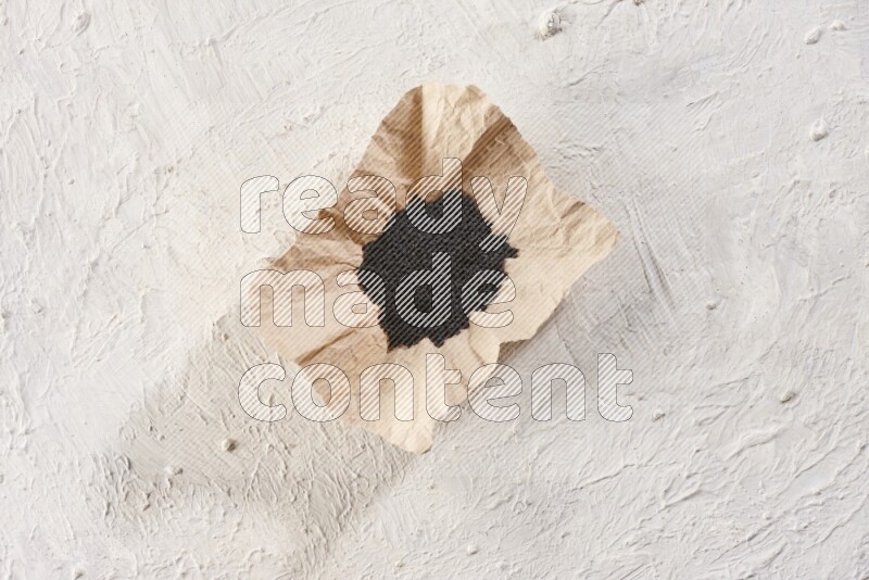 A crumpled piece of paper full of black seeds on a textured white flooring