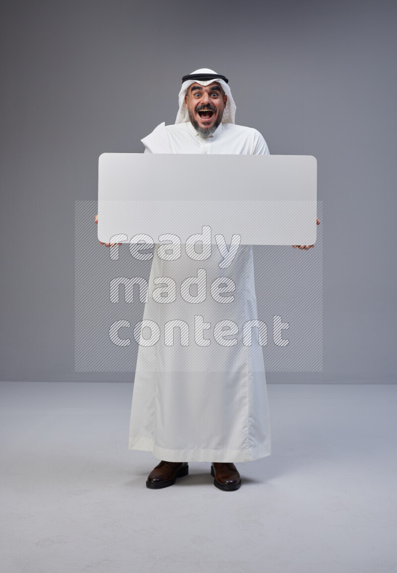 Saudi man Wearing Thob and white Shomag standing holding board on Gray background
