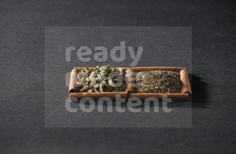 مربعان من أعواد القرفة ممتلئان بحبوب الكمون وحبوب الهيل علي خلفية سوداء