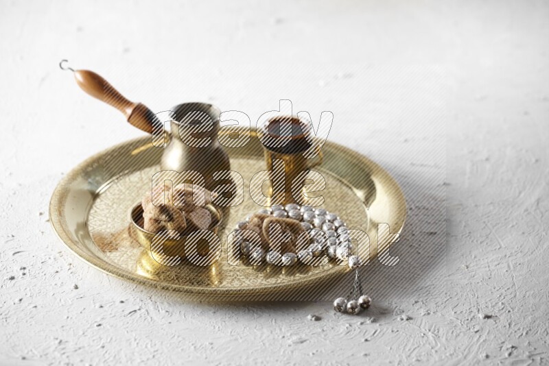Dried figs in a metal bowl with coffee and prayer beads on a tray in a light setup
