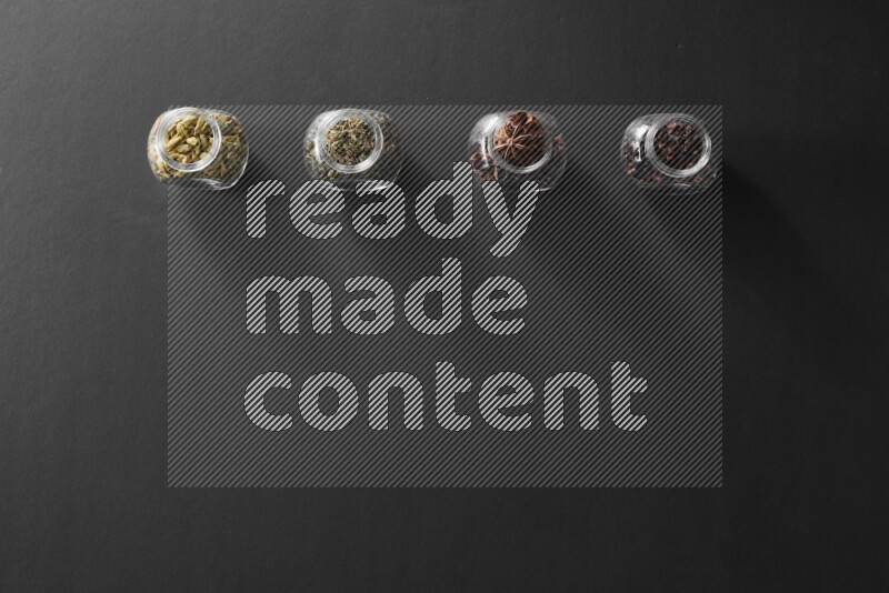 قرنفل وحبوب الهيل وريحان مجفف ويانسون نجمي في أوعية زجاجية علي خلفية سوداء