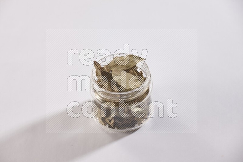 A glass jar filled with dried bay leaves on white flooring