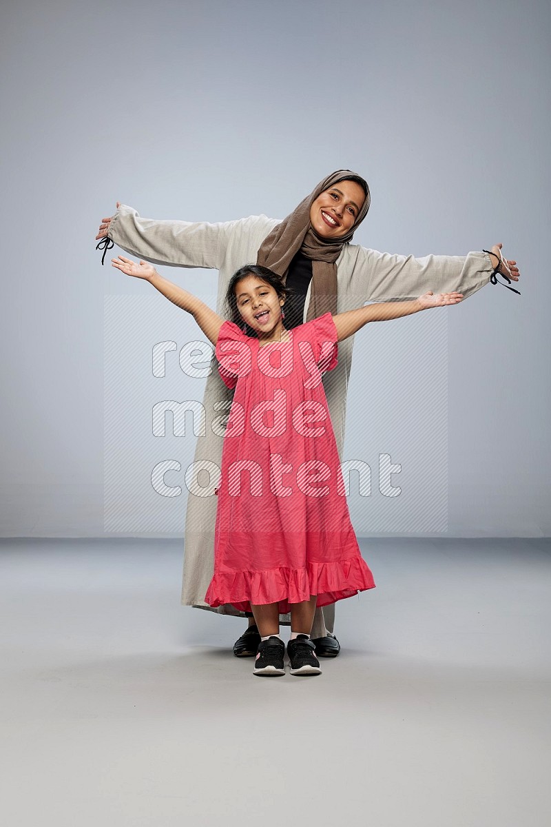 A girl and her mother interacting with the camera on gray background