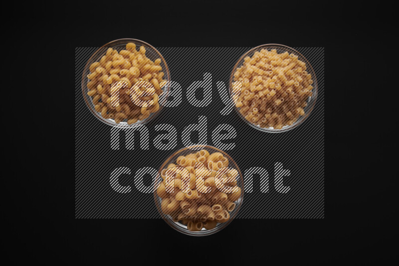 Different pasta types in glass bowls on black background