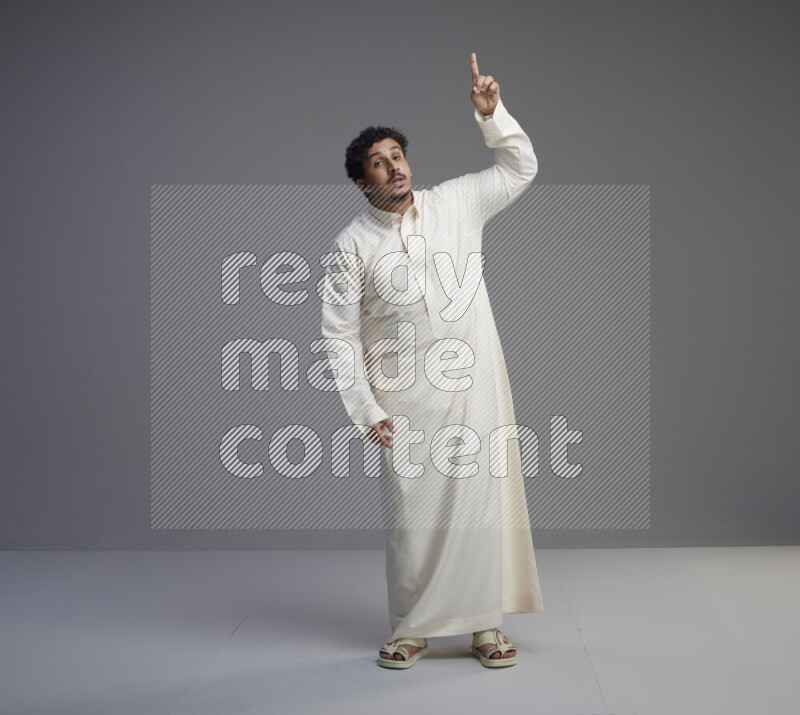 A Saudi man standing wearing thob interacting with the camera on gray background