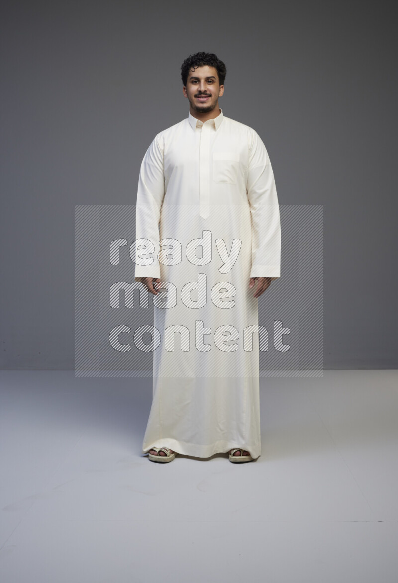 A Saudi man standing wearing thob interacting with the camera on gray background