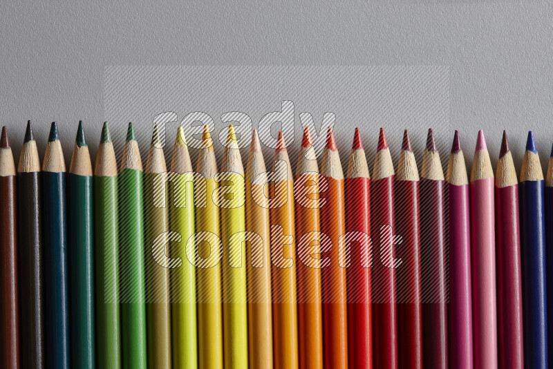 A collection of colored pencils arranged showcasing a gradient of different hues on grey background