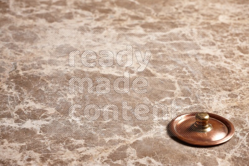 A small copper pot lid on beige marble background