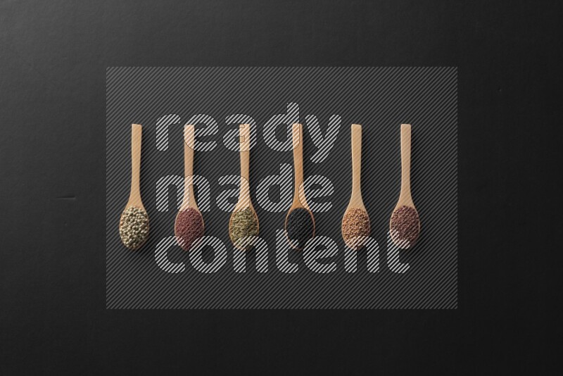 الفلفل الأسود وحبوب الخردل وحبة البركة وحب الرشاد والكمون و حبوب الكتان في معالق خشبية علي خلفية سوداء