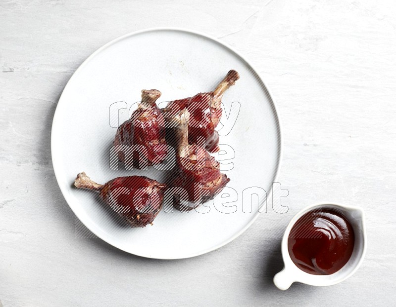 drumstick wrapped in bacon on round white ceramic plate on grey textured countertop