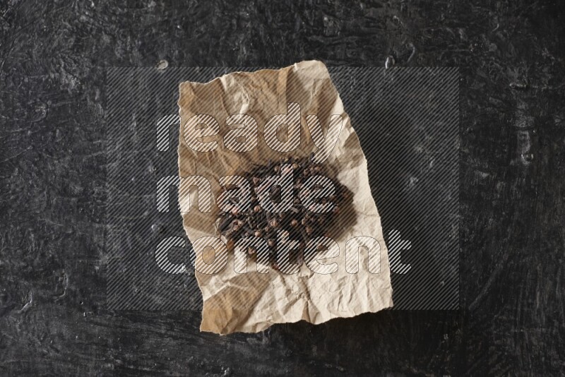 Cloves in crumpled piece of paper on a textured black flooring