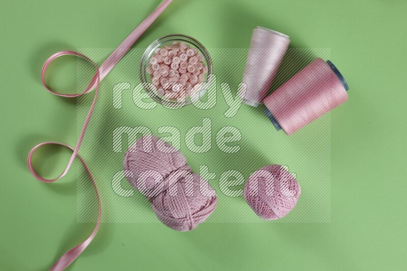 A pink collection of sewing and tailoring tools arranged on a green background