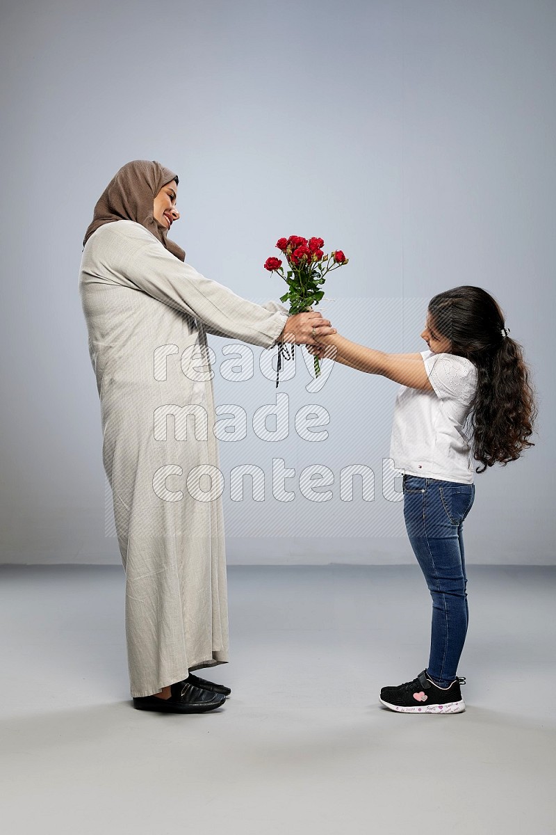 A girl standing giving flowers to her mother on gray background