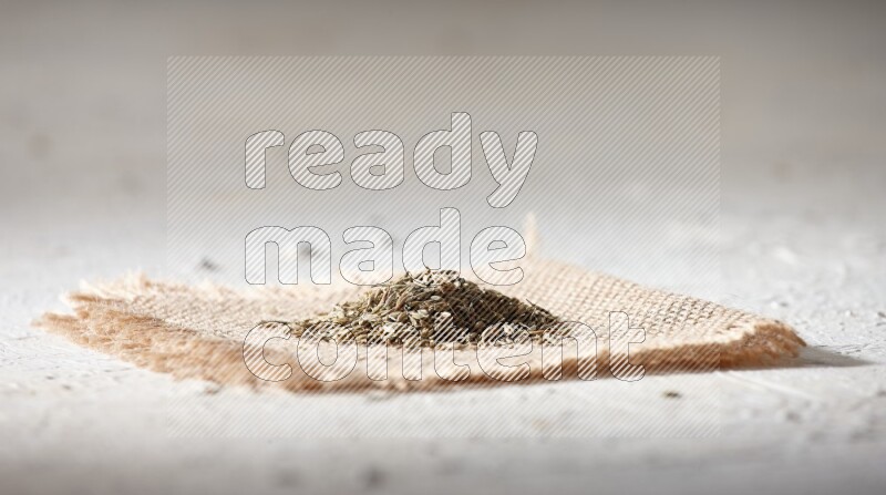 Cumin seeds on a burlap piece on a textured white flooring