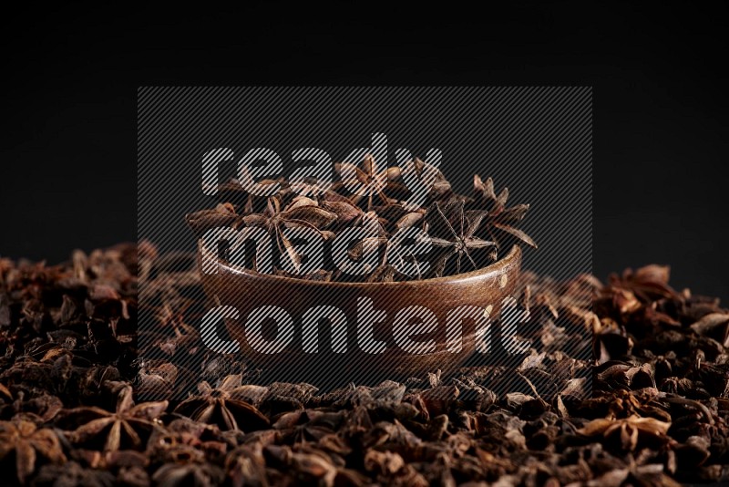 Star Anise in a wooden bowl and surrounded by more anise filling the frame on black flooring