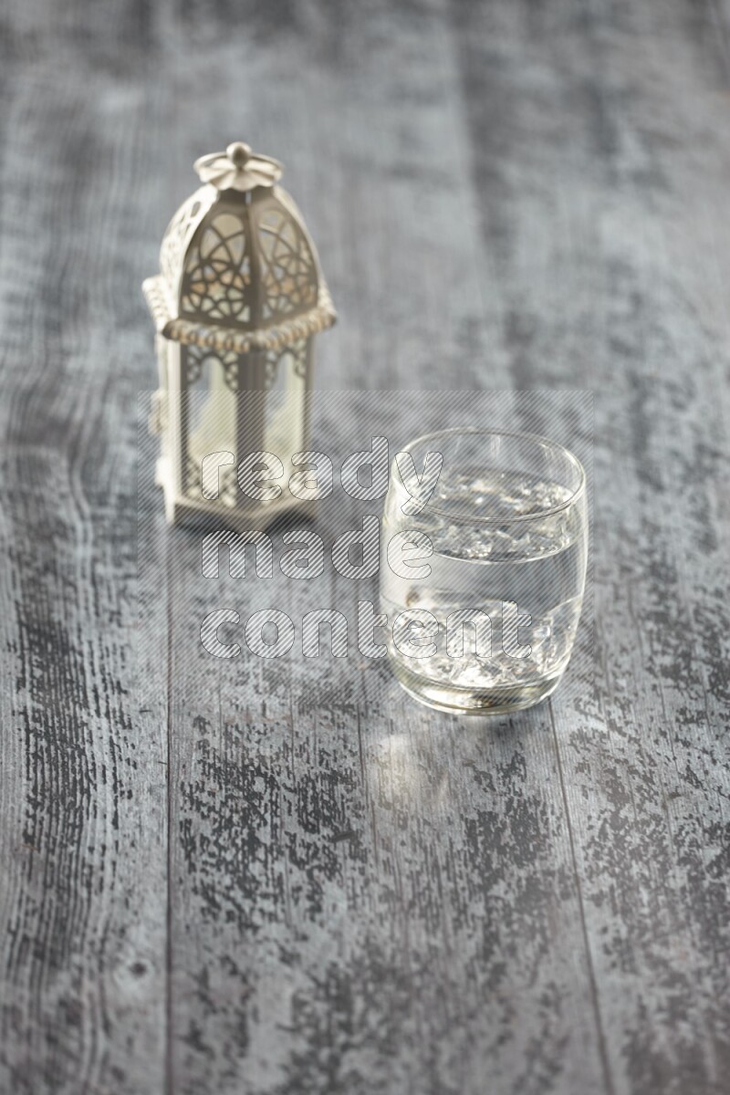 A white lantern with different drinks, dates, nuts, prayer beads and quran on grey wooden background
