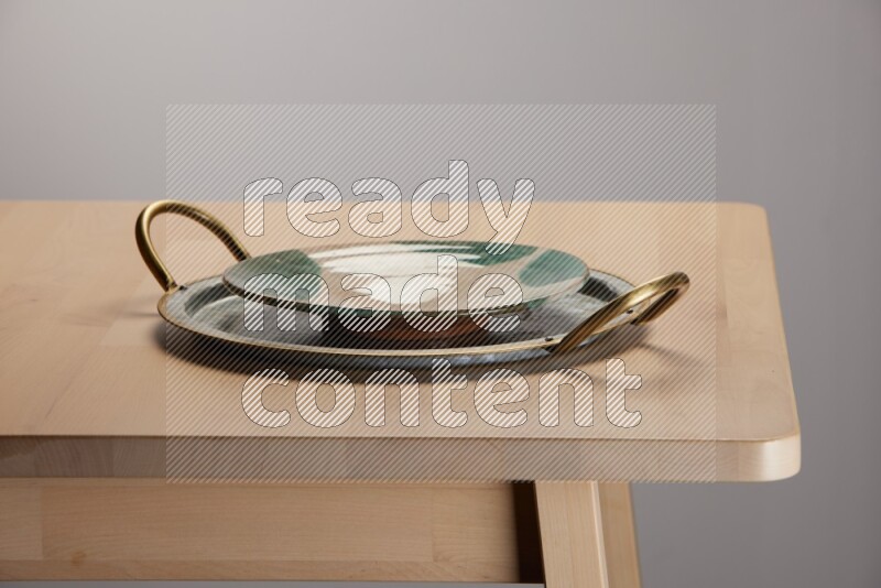 multicolored plate placed on a rounded stainless steel tray with golden handels on the edge of wooden table