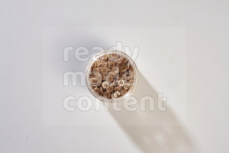 A glass jar full of colored buttons on grey background