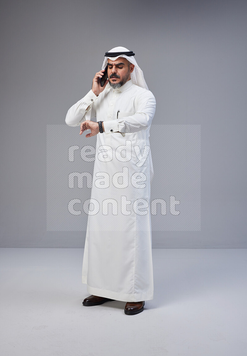 Saudi man Wearing Thob and white Shomag standing talking on phone on Gray background