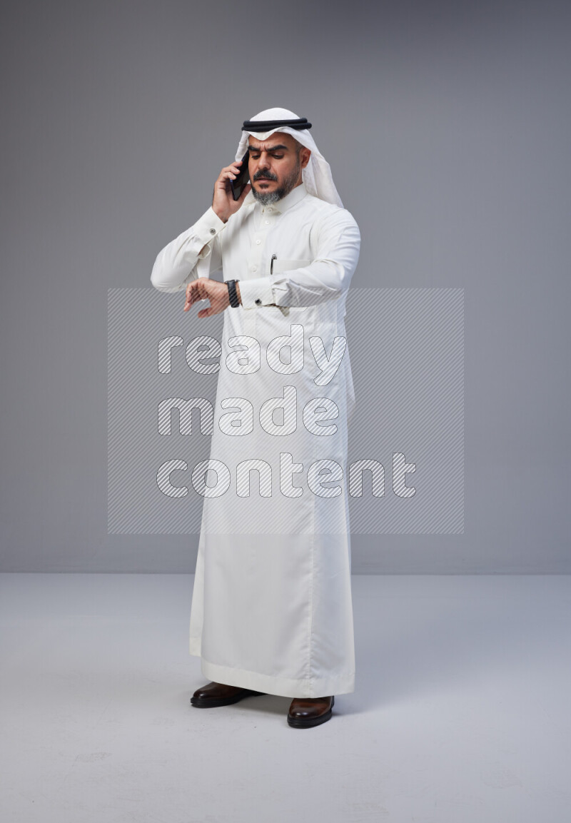 Saudi man Wearing Thob and white Shomag standing talking on phone on Gray background