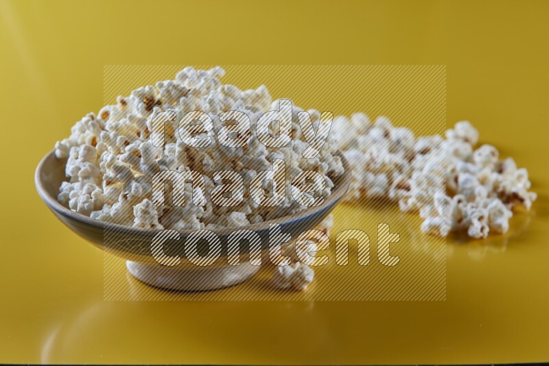 A multicolored ceramic plate full of popcorn with popcorn beside it on a yellow background in different angles