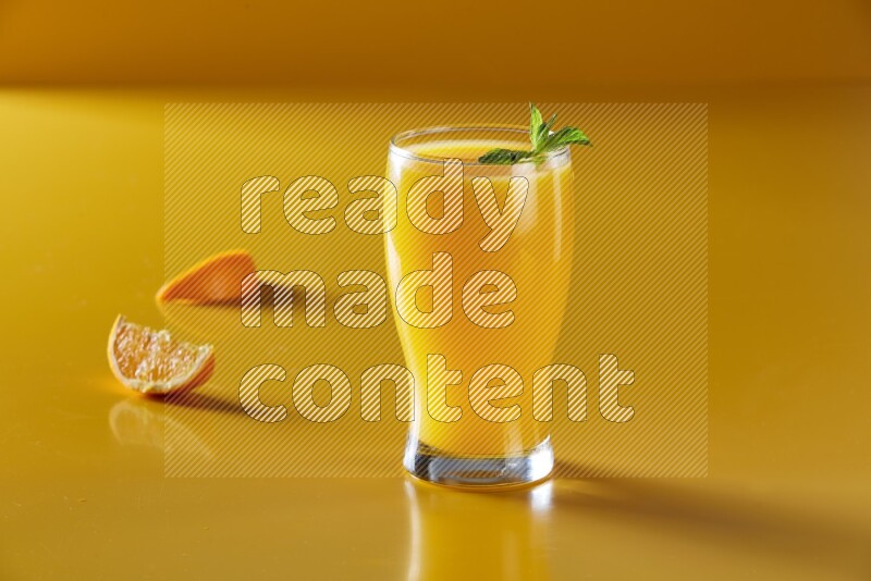 glass of orange juice with  mint on yellow background