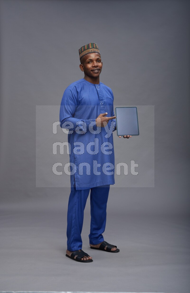 Man wearing Nigerian outfit standing showing tablet to camera on gray background