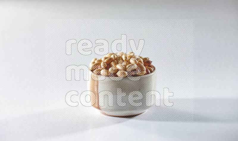 A beige ceramic bowl full of peeled peanuts on a white background in different angles