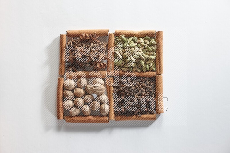 4 مربعات من أعواد القرفة ممتلئة بالهيل واليانسون والقرنفل وجوزة الطيب على أرضية بيضاء