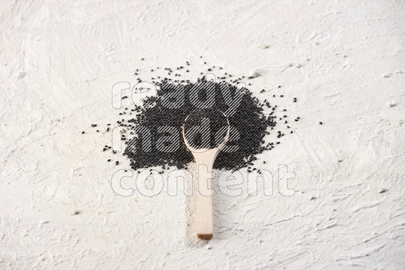 A wooden spoon full of black seeds on textured white flooring