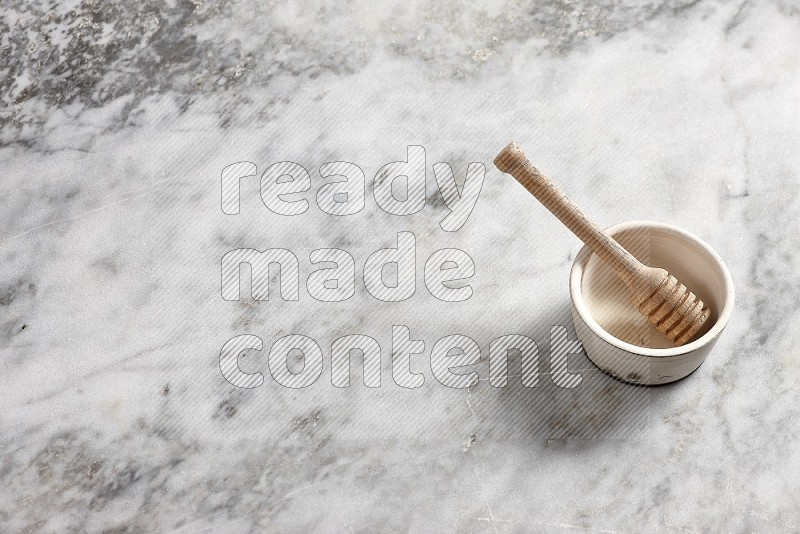 White Pottery Bowl with wooden honey handle in it, on grey marble flooring, 65 degree angle