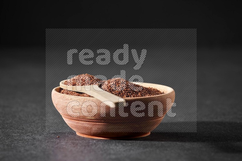 A wooden bowl full of garden cress seeds and a wooden spoon full of the seeds on it on a black flooring