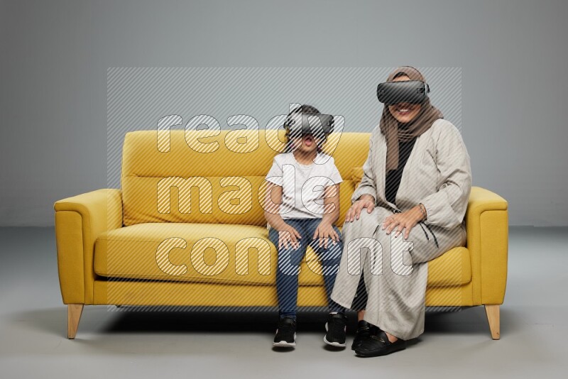 A girl and her mother sitting playing with VR on gray background