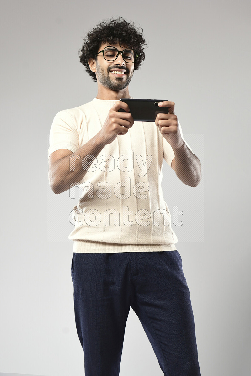 A man wearing casual standing and gaming on the phone on white background