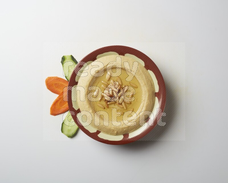 Hummus in a traditional plate garnished with pine nuts on a white background