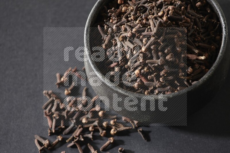 A black pottery bowl full of cloves on a black flooring