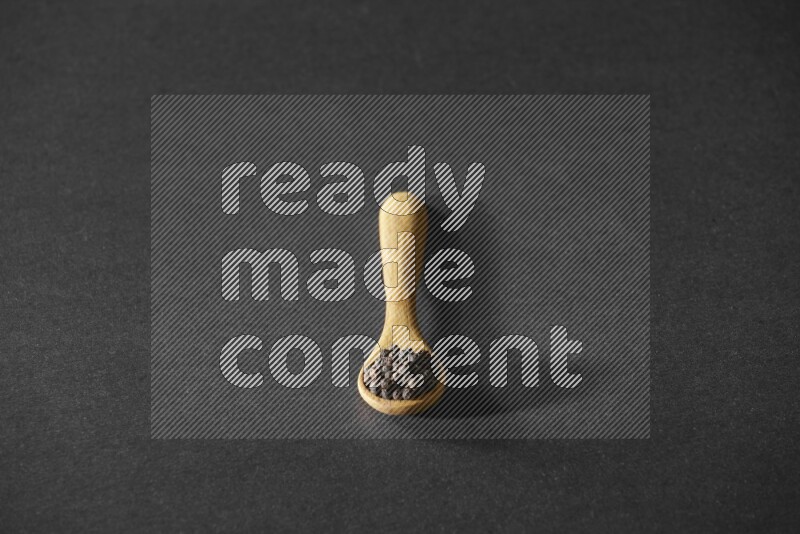 حبوب الفلفل الأسود في ملعقة خشبية علي خلفية سوداء