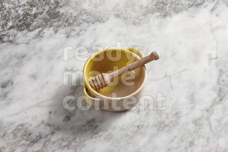 Multicolored Pottery bowl with wooden honey handle in it, on grey marble flooring, 65 degree angle