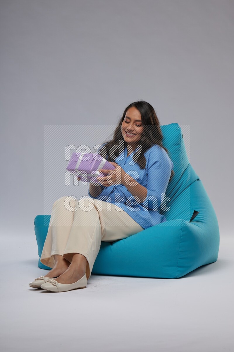 A woman sitting on a blue beanbag and holding a gift