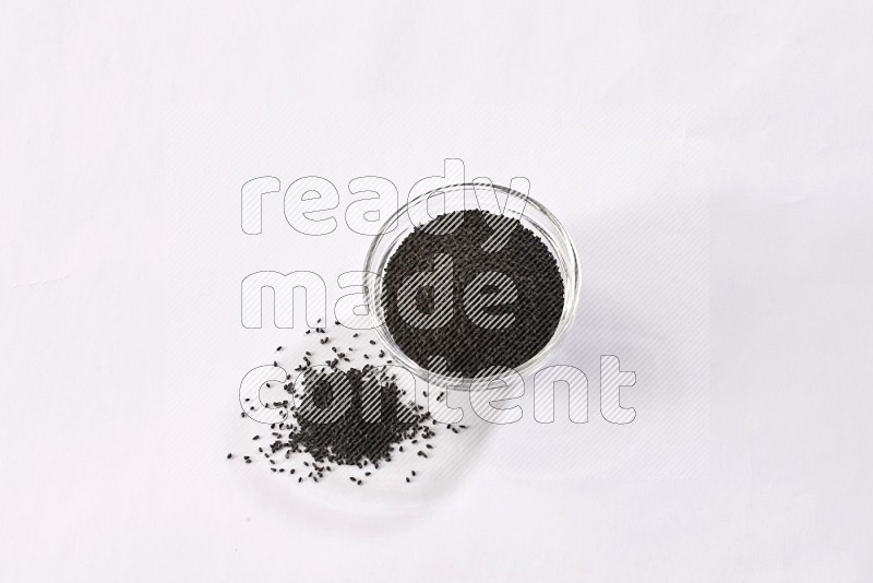 A glass bowl full of black seeds and some more spread next to it on a textured white flooring in different angles