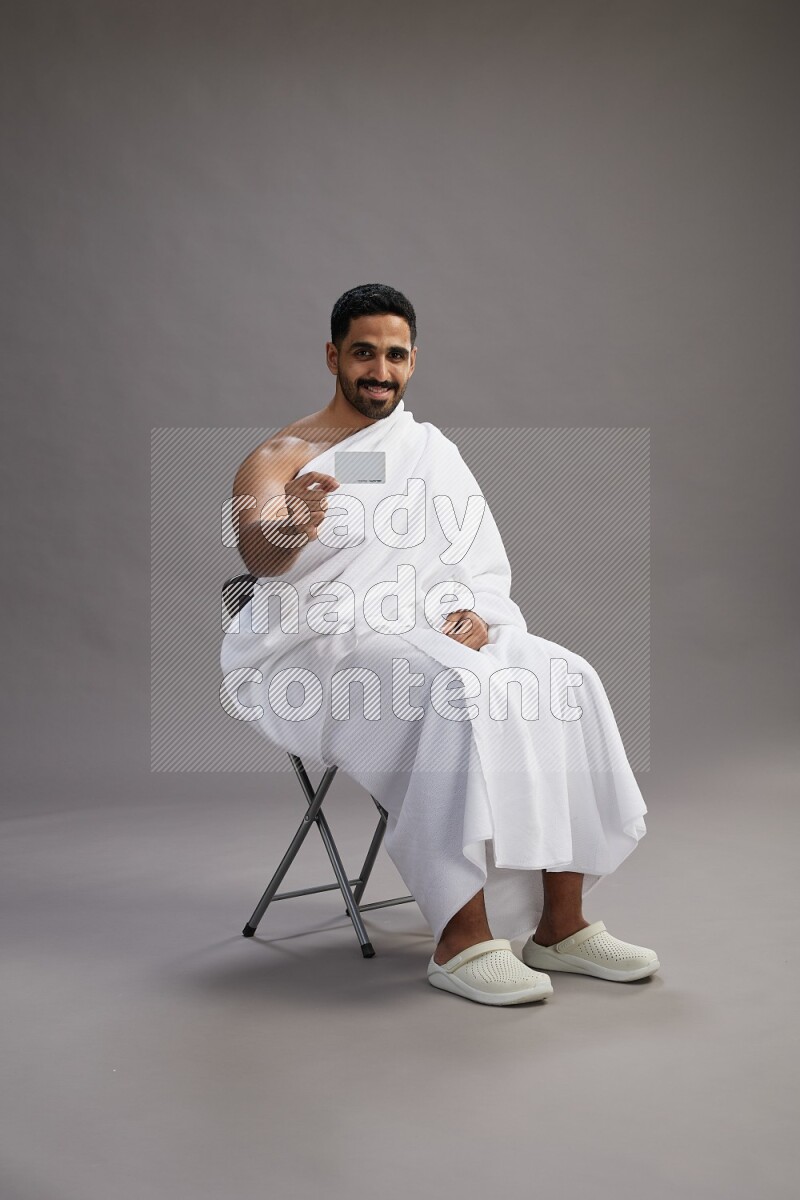A man wearing Ehram sitting on chair holding ATM card on gray background
