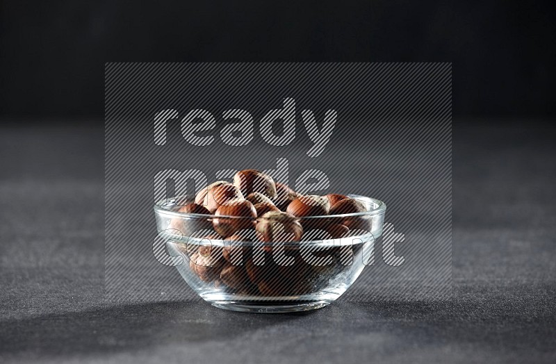 A glass bowl full of hazelnuts on a black background in different angles