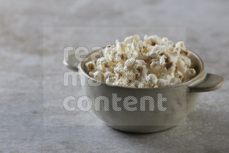 popcorn in a off-white handheld ceramic bowl on a grey textured countertop
