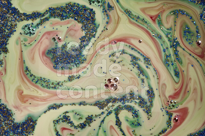 A close-up of sparkling blue and gold glitter scattered on swirling green and red background