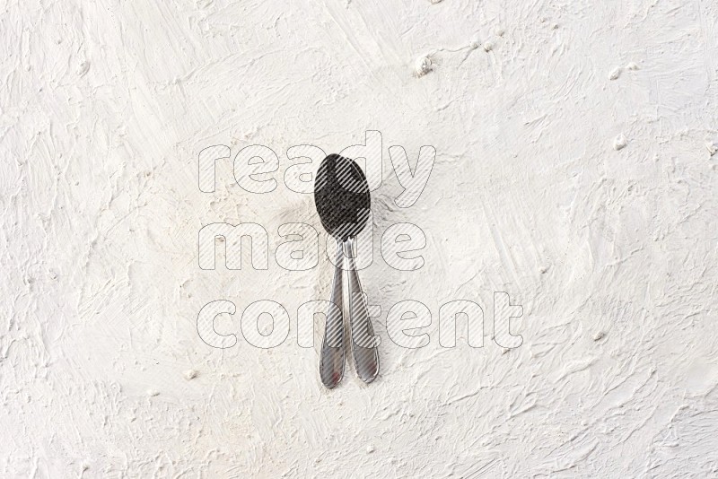 2 metal spoons full of black seeds on textured white flooring